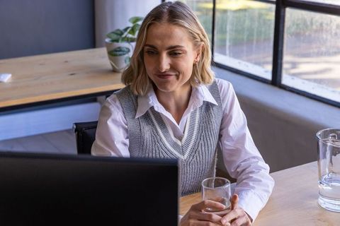 Professional woman working with computer and holding glass of water