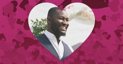 Smiling groom standing in heart frame with floral canopy and pink heart background