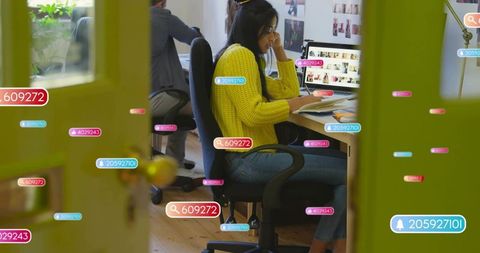 Woman in yellow sweater working at open-plan office surrounded by digital notifications
