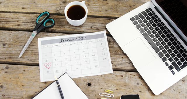 A calendar with a heart around a date suggests planning for a special event, with copy space. Surrounding the calendar are a laptop, coffee cup, and office supplies, indicating a work or home office environment.