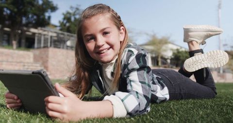 Smiling girl using tablet while relaxing on grass