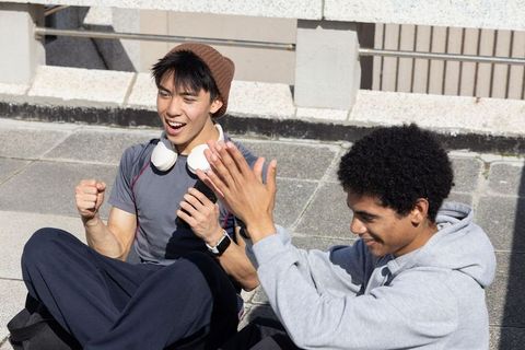 Diverse teenage male friends celebrating and high-fiving while relaxing on sunlit urban rooftop