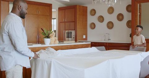 African american father and son building blanket fort and bonding in bright modern kitchen