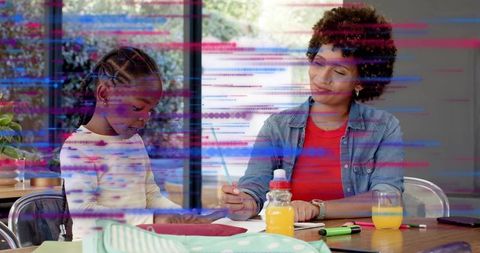 Parent guiding child with homework at bright home table holding pencil, tutoring moment