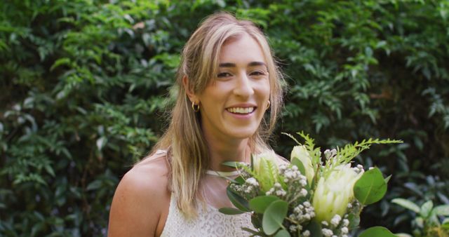Portrait of happy caucasian woman holding bunch of flowers in garden on sunny day. wedding day and celebration concept.