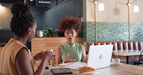 Two professionals collaborating over laptop and coffee during casual coworking cafe meeting