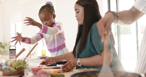 African american mother and daughter cooking together in bright kitchen making fresh meal