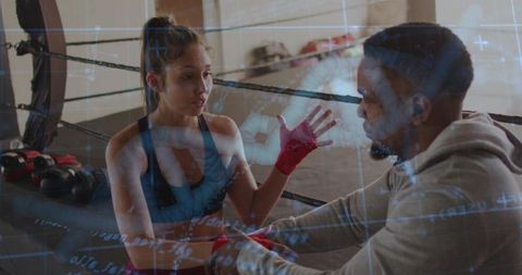 Boxing trainer adjusting red hand wraps while athlete prepares in ring with blue data overlay