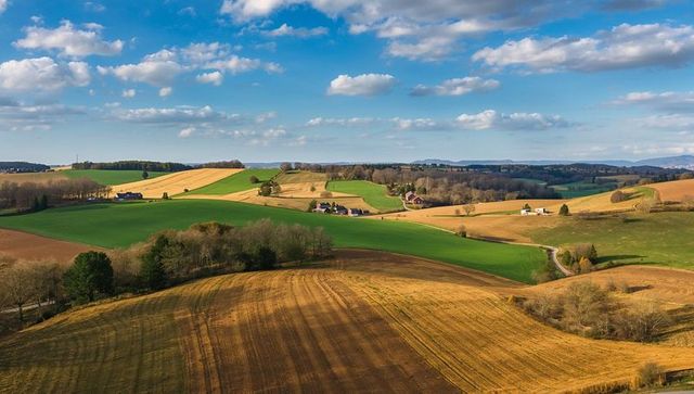 Rolling patchwork farmland with green pastures, harvested fields and winding country lane