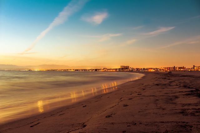 Serene Sunset Over Coastal Beach with City Lights in Distance - Download Free Stock Photos Pikwizard.com