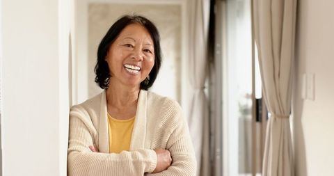 Senior asian woman enjoying relaxation at home near light grey curtains
