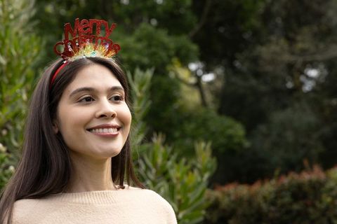 Smiling woman wearing red merry christmas headband in lush garden portrait