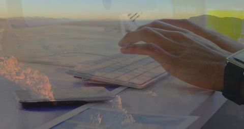 Right hand typing on slim keyboard with desert double exposure, minimal warm workspace