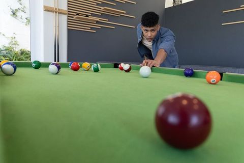 African american teen leaning over pool table aiming cue ball in modern game room