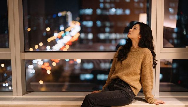 Contemplative asian woman gazing out high-rise window at night with bokeh city lights
