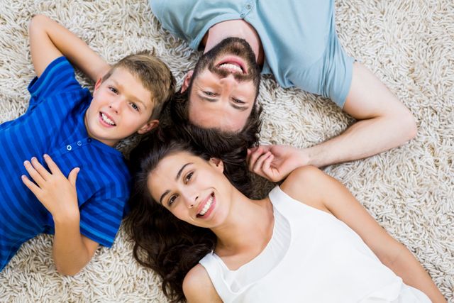 Family enjoying quality time together at home, lying on a soft rug and smiling. Perfect for use in advertisements, family-oriented content, lifestyle blogs, and parenting articles.