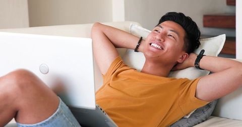 Relaxed Asian Man Smiling with Laptop at Home