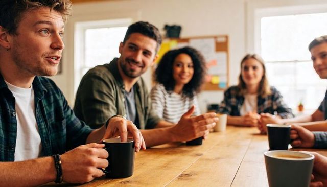 Casual team meeting sharing ideas over coffee at wooden table in collaborative workspace