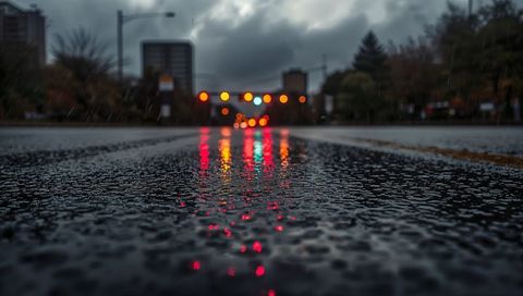 Wet urban asphalt reflecting neon traffic lights and bokeh puddles at rainy dusk city street