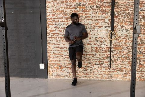 African american man balancing on one leg holding jump rope in industrial brick gym studio