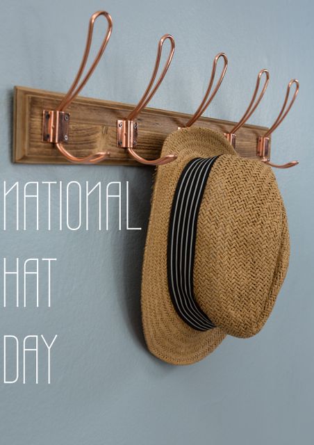 Straw hat hanging on stylish wooden wall hooks with copper accents on a gray wall. The image includes text 'National Hat Day' on the left. Suitable for home decor websites, blogs about rustic or farmhouse style interiors, and promotional materials for National Hat Day or hat-related events.