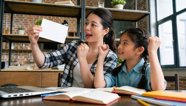 Asian mother and daughter celebrating study success at home holding blank card and cheering