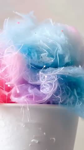 Shifting camera capturing pastel cotton candy shedding delicate fibers over ceramic cup