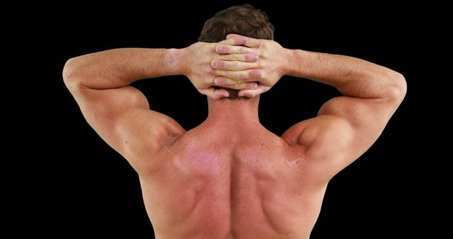 Man showcasing his well-defined back muscles while holding hands behind head against black background. Ideal for fitness magazines, workout routines, bodybuilding websites, and physical therapy advertisements.