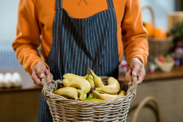 Mid section of vendor holding a basket of fresh bananas, ideal for use in marketing materials for farmers' markets, grocery stores, or healthy eating campaigns. Highlights the freshness and quality of organic produce, perfect for promoting local agriculture and sustainable food practices.