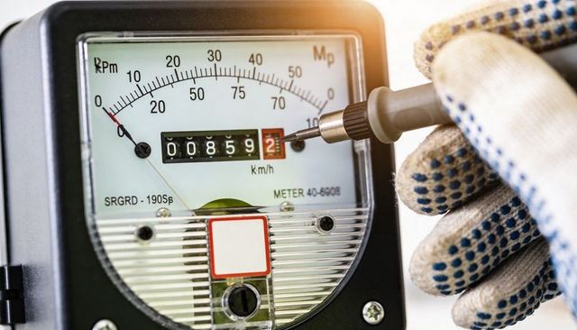 Gloved technician calibrating analog odometer meter closeup showing 00859 reading