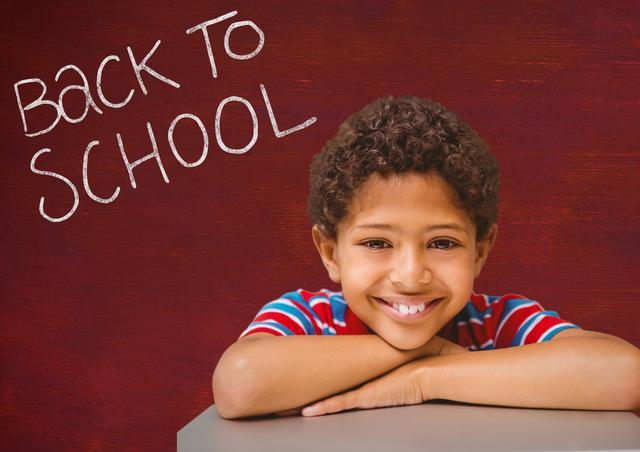 Portrait of happy boy leaning on table with back to school text against colored background
