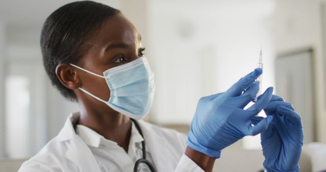 African american female doctor wearing face mask preparing covid vaccine for patient. medical healthcare professional at work during coronavirus covid 19 pandemic.