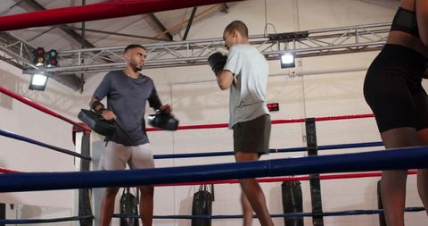 Boxing coach training student with focus pads in ring as female trainee practicing footwork