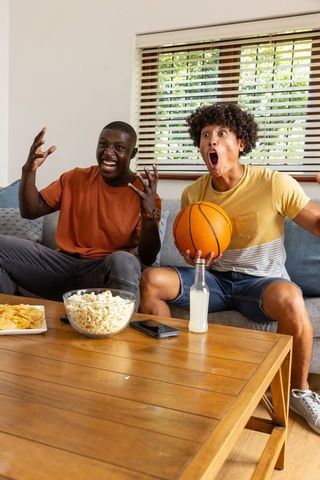 Cheering diverse friends watching basketball at home with popcorn and basketball