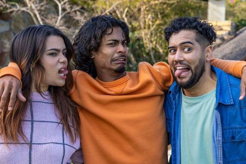Diverse friends making faces and linking arms in backyard playful multicultural trio