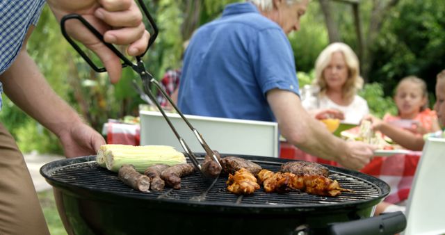 Family barbecue in a garden with various grilled meats and corn. Perfect for use in promotional materials for summer events, grilling tips, family gatherings, outdoor activities, and barbecue recipes.