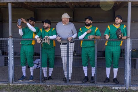Veteran coach leading amateur baseball team in dugout with players in green uniforms