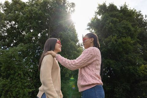 Sharing sunny moment in park: two friends wearing red sunglasses and cozy sweaters