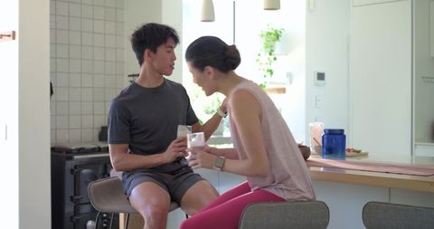 Young couple sitting at breakfast bar sharing smoothie in bright modern minimalist kitchen