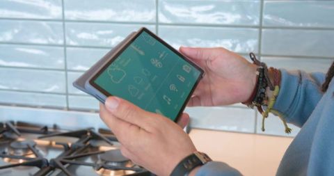 Mid-adult man controlling smart kitchen with tablet at gas stove and modern backsplash