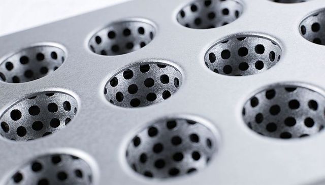 Macro close-up metallic perforated plate with countersunk circular recesses and grid pattern
