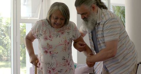Elder man assisting senior woman with walking cane for mobility support