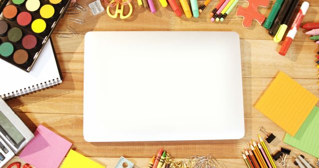 Overhead view of a desk filled with colorful school supplies surrounding a blank tablet screen. This image is great for themes related to education, back to school, creativity, and technology integration in learning. It can be used in blogs, educational websites, back-to-school advertisements, and articles on creative productivity.