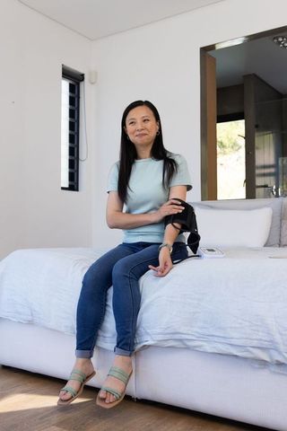 Mature african american woman checking wearable blood pressure cuff while sitting on bed