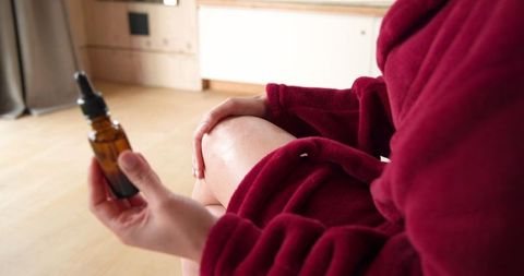 Woman in Bathrobe Applying Oil From Amber Bottle Spa Wellness