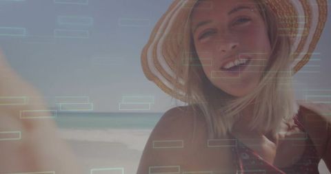 Smiling woman wearing wide-brim straw hat holding phone at sunlit beach with hud overlay
