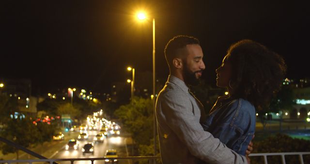Romantic diverse couple smiling and embracing in city street at night, copy space. City living, romance, love, relationship, free time and lifestyle, unaltered.