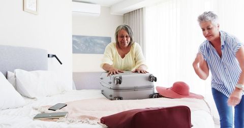 Senior Lesbian Couple Packing Bags for Summer Vacation in Bedroom