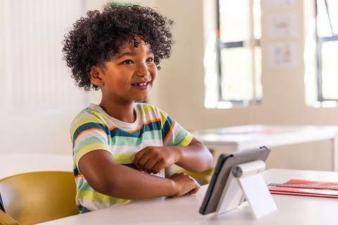 Smiling african american boy using tablet at classroom desk engaging with educational app