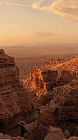 Vertical drone pan at sunset revealing layered sandstone canyon and dramatic desert cliffs